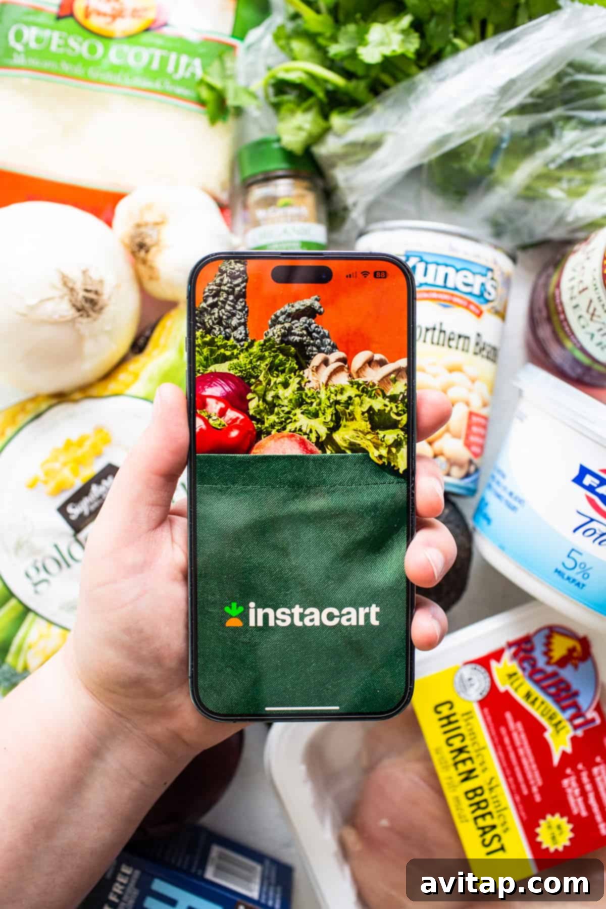 A person holding a phone with grocery bags visible in the background, showcasing the convenience of Instacart.