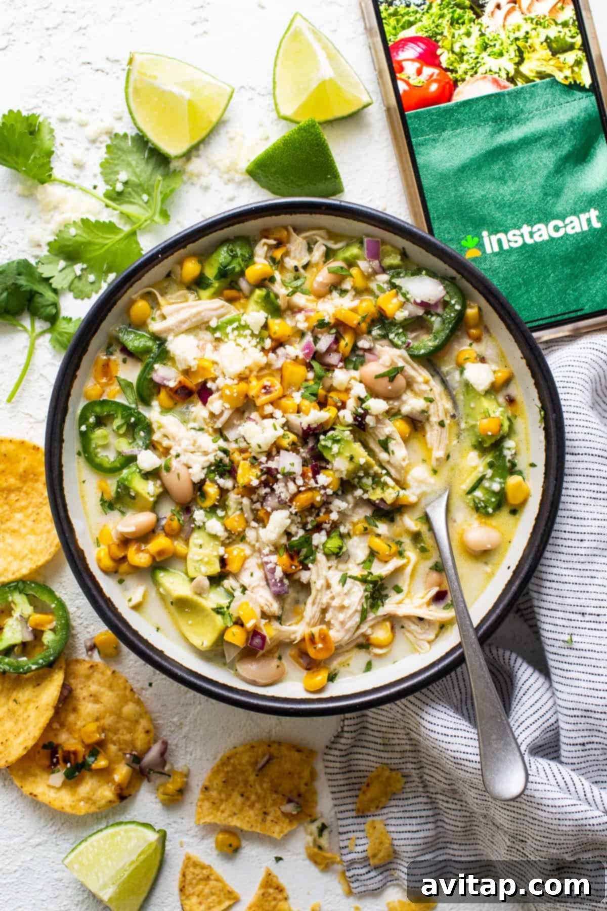 A vibrant bowl of Street Corn Chicken Chili, topped with fresh avocado, cilantro, and served with a side of tortilla chips and lime wedges.