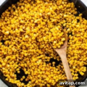 Corn kernels being browned in a cast iron skillet with a wooden spoon, indicating a smoky flavor development.