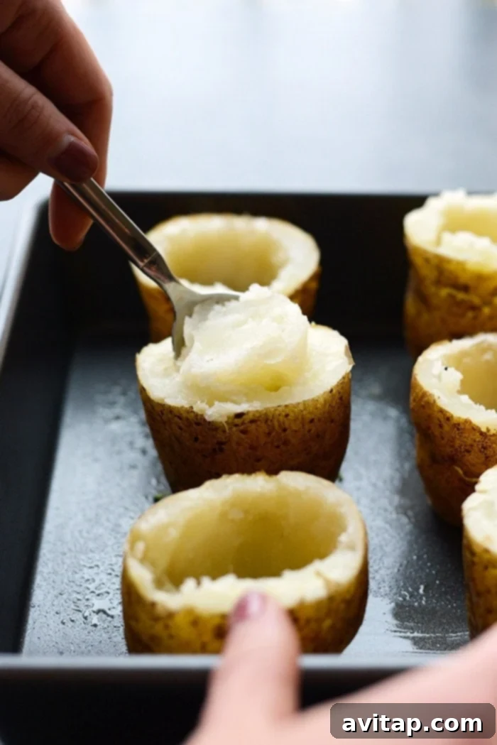 Scooping out the fluffy interior of a baked potato to prepare the creamy filling for Lightened Up Broccoli Cheddar Twice Baked Potatoes.