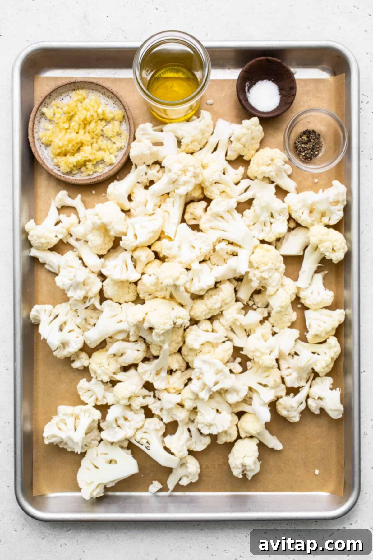 Cauliflower florets arranged neatly in a single layer on a parchment-lined baking sheet, prepared for roasting.