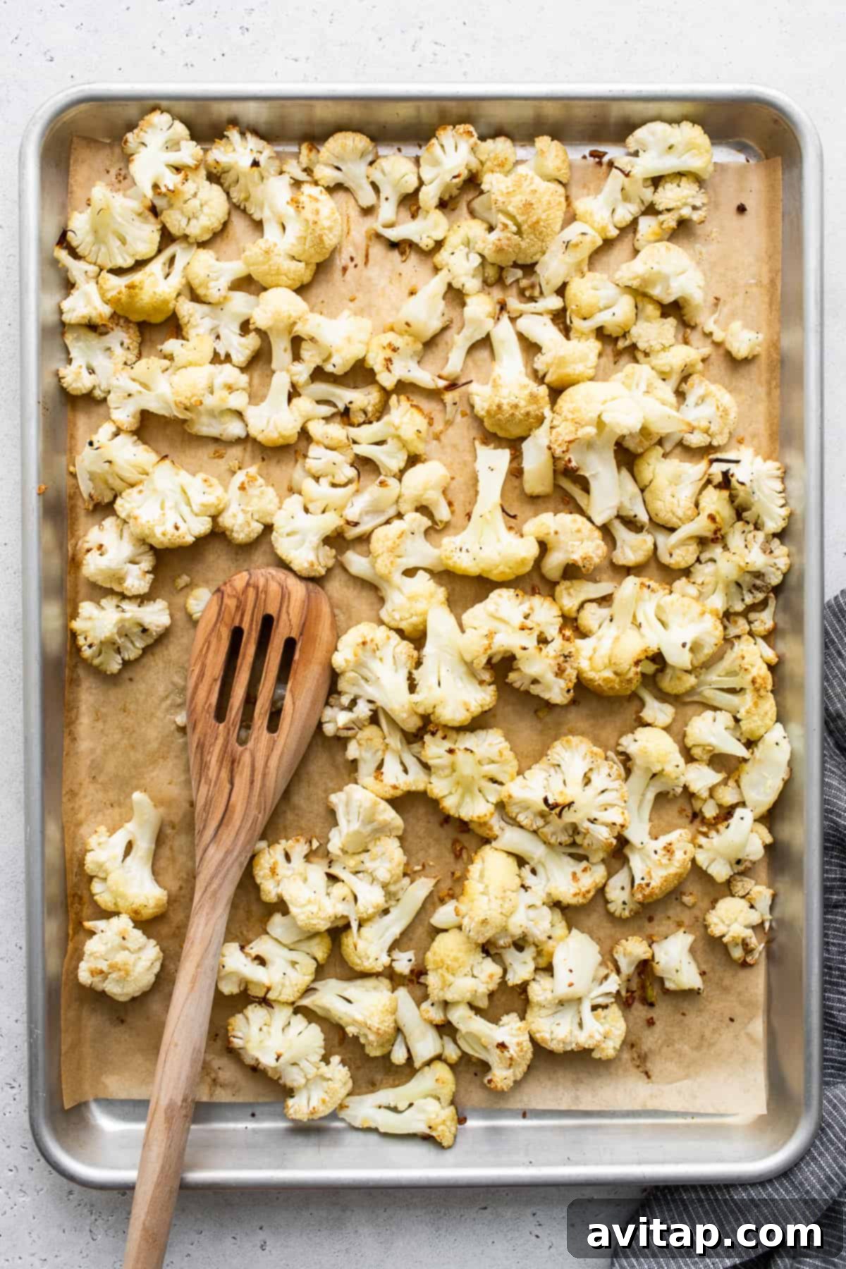Crispy, golden-brown roasted cauliflower florets spread on a parchment-lined baking sheet after roasting, showing perfect caramelization.