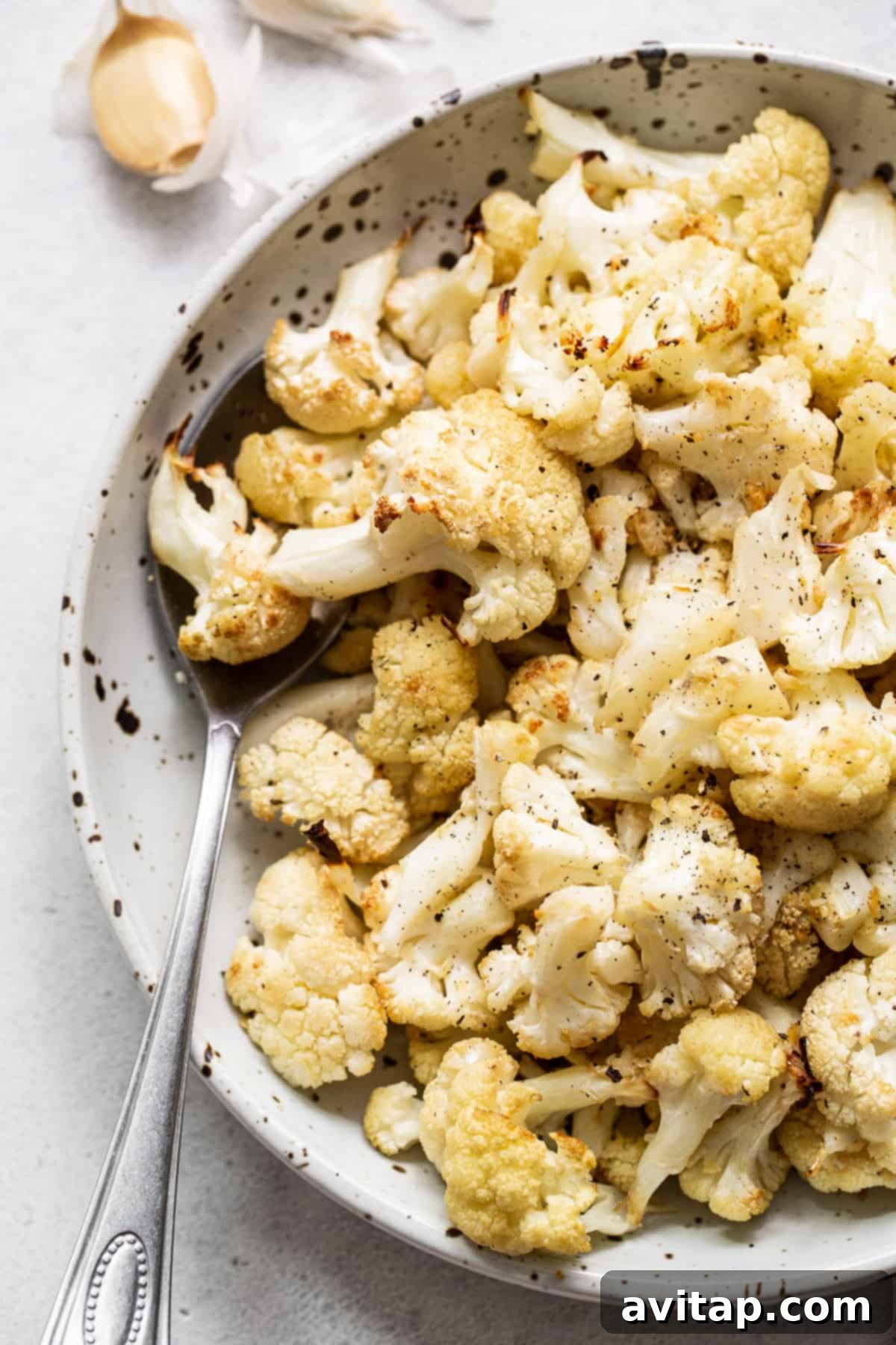 Roasted cauliflower served in a bowl with a serving spoon, garnished, and ready to eat.
