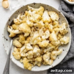 Roasted cauliflower in a bowl, showing golden-brown florets with garlic and fresh herbs. 