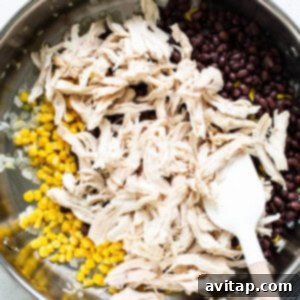 Chicken and corn in a pan with a wooden spoon.
