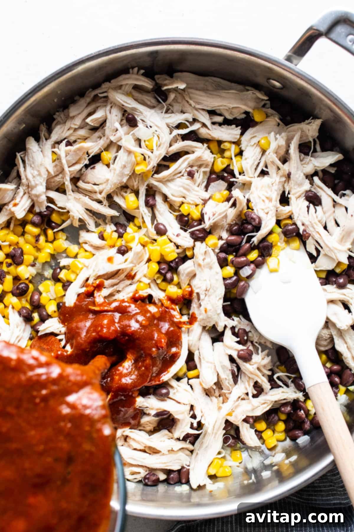 Chicken and corn simmering in a pan with rich enchilada sauce.