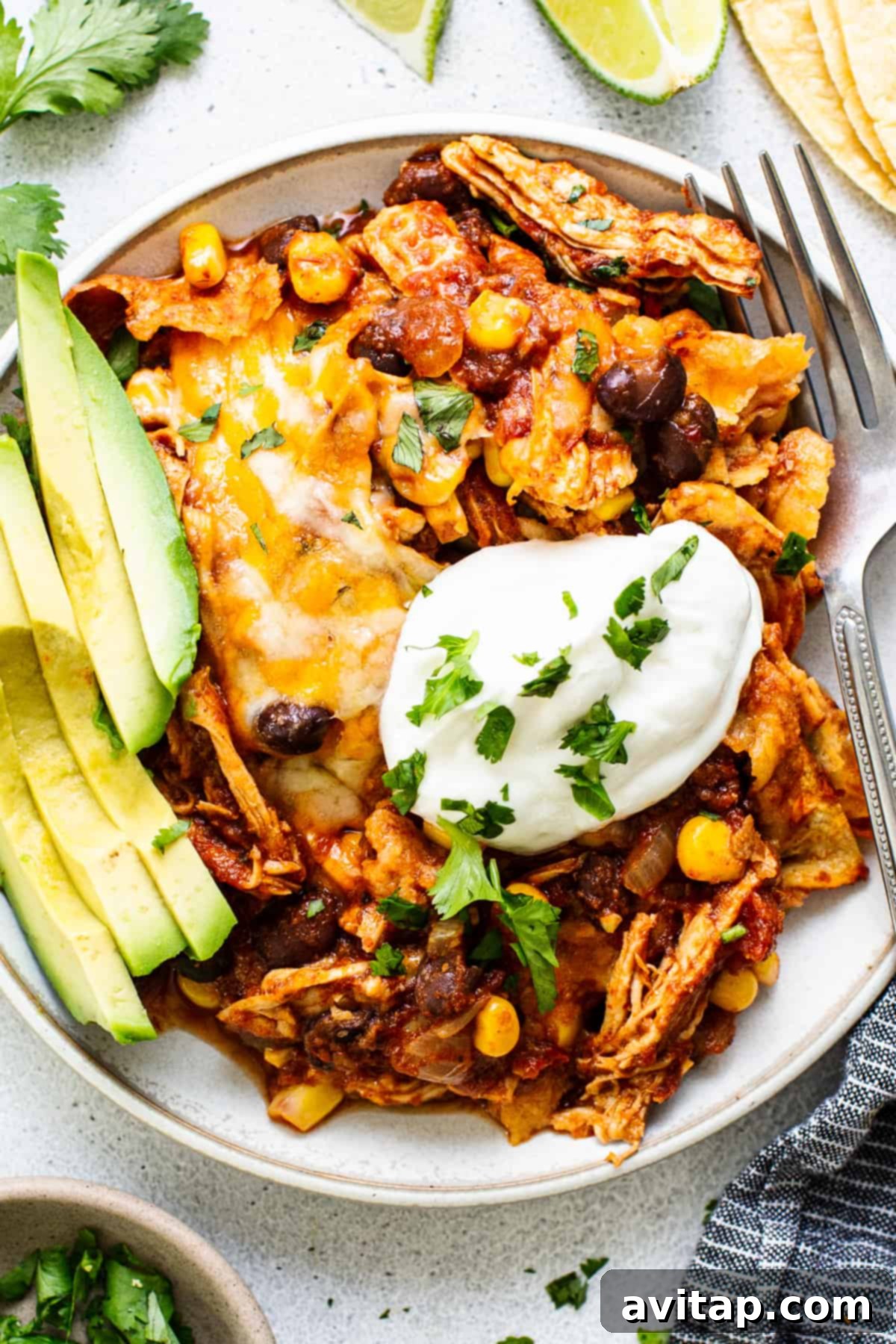 Mexican chicken enchilada served on a plate with sour cream and avocado.