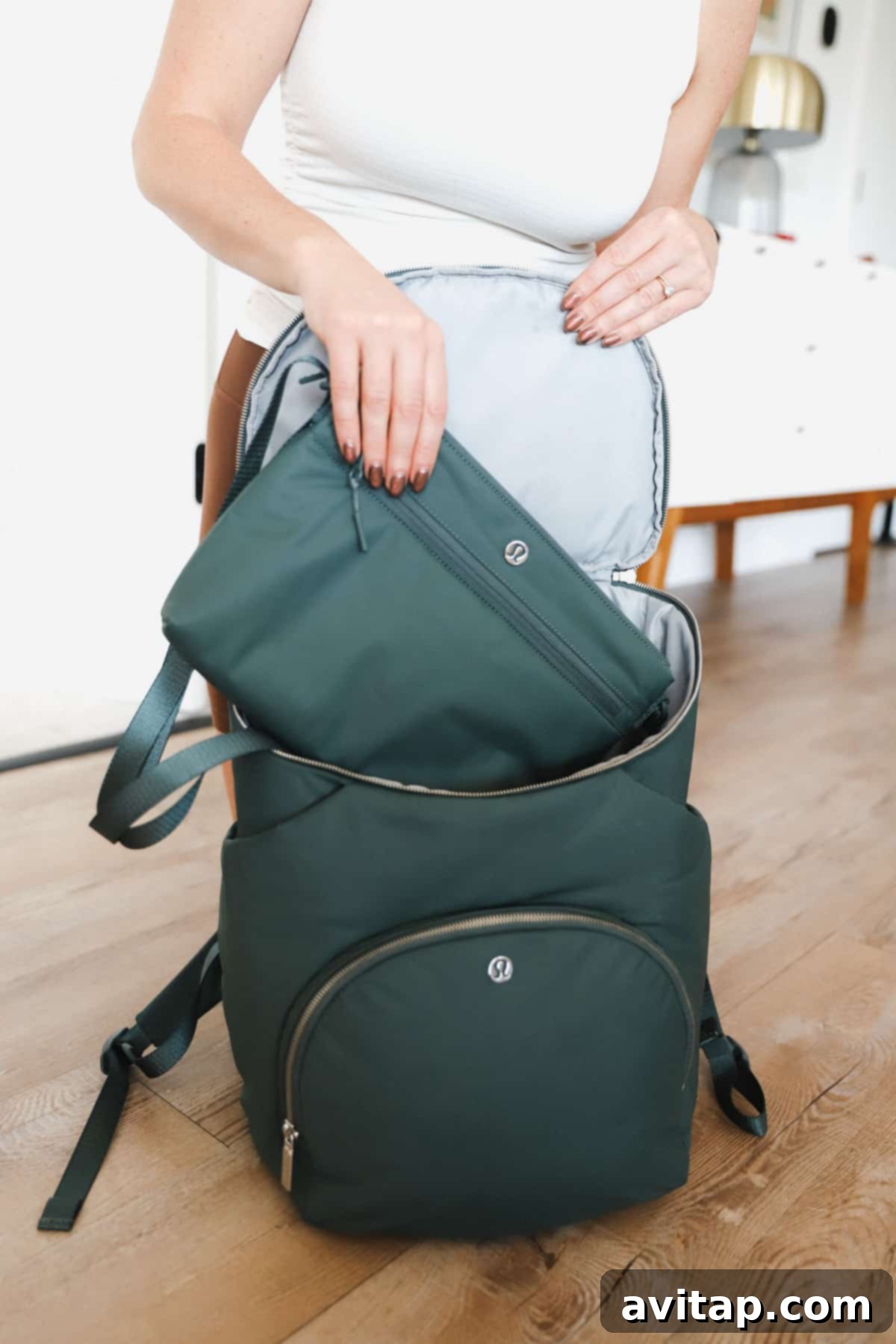 A detailed view of a woman holding the Lululemon New Parent Backpack, showcasing its two main zippered compartments and the quality of the fabric.