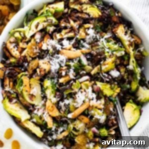 A bowl of brussels sprout salad with nuts and raisins.