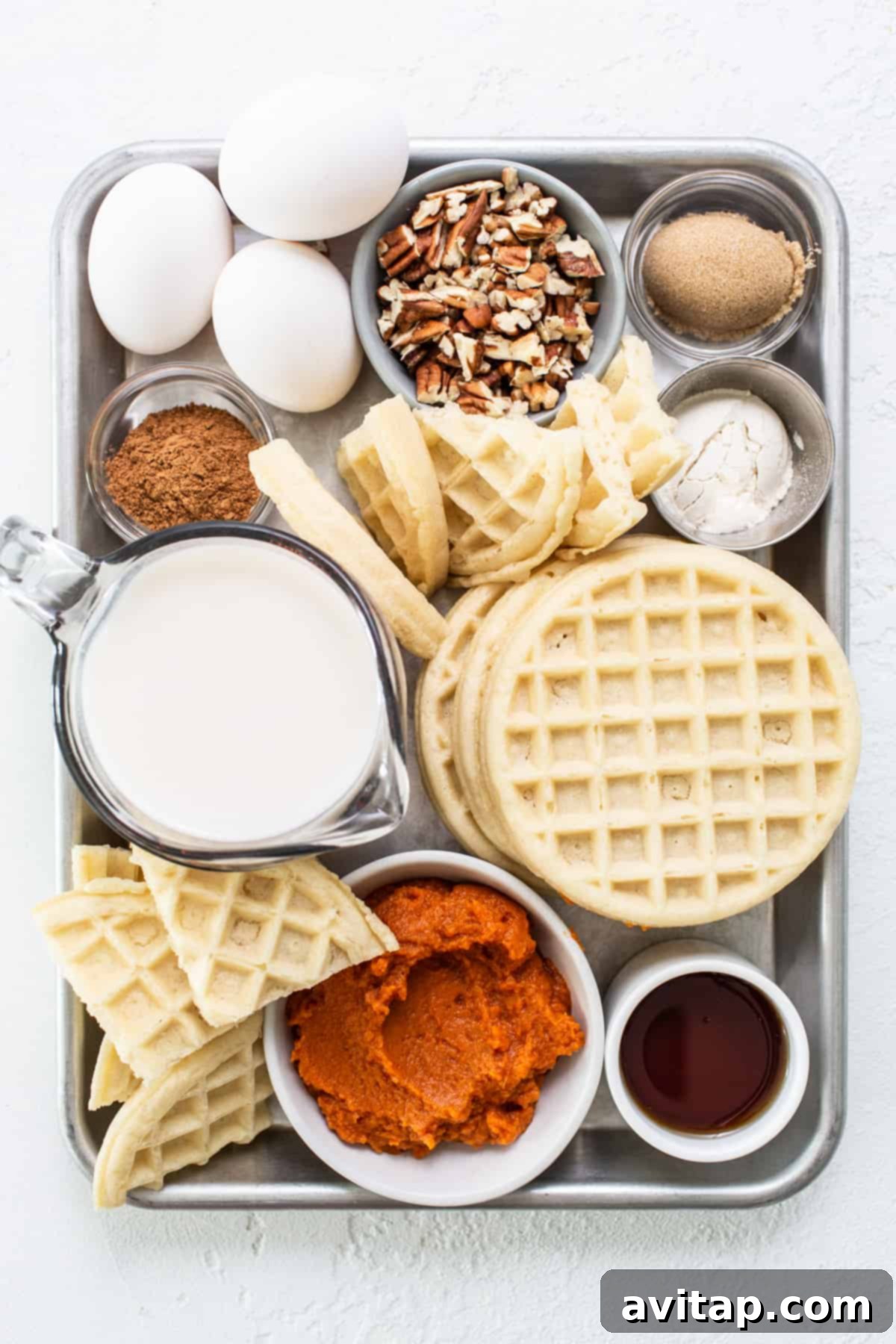 An array of fresh ingredients for pumpkin waffle casserole, including waffles, eggs, milk, and spices, neatly arranged on a tray.