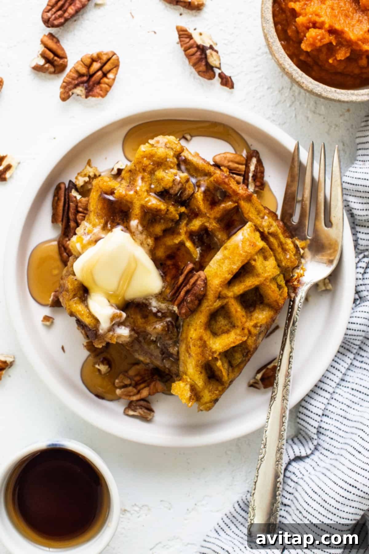 A serving of pumpkin waffles, beautifully presented with butter and chopped pecans on a plate.