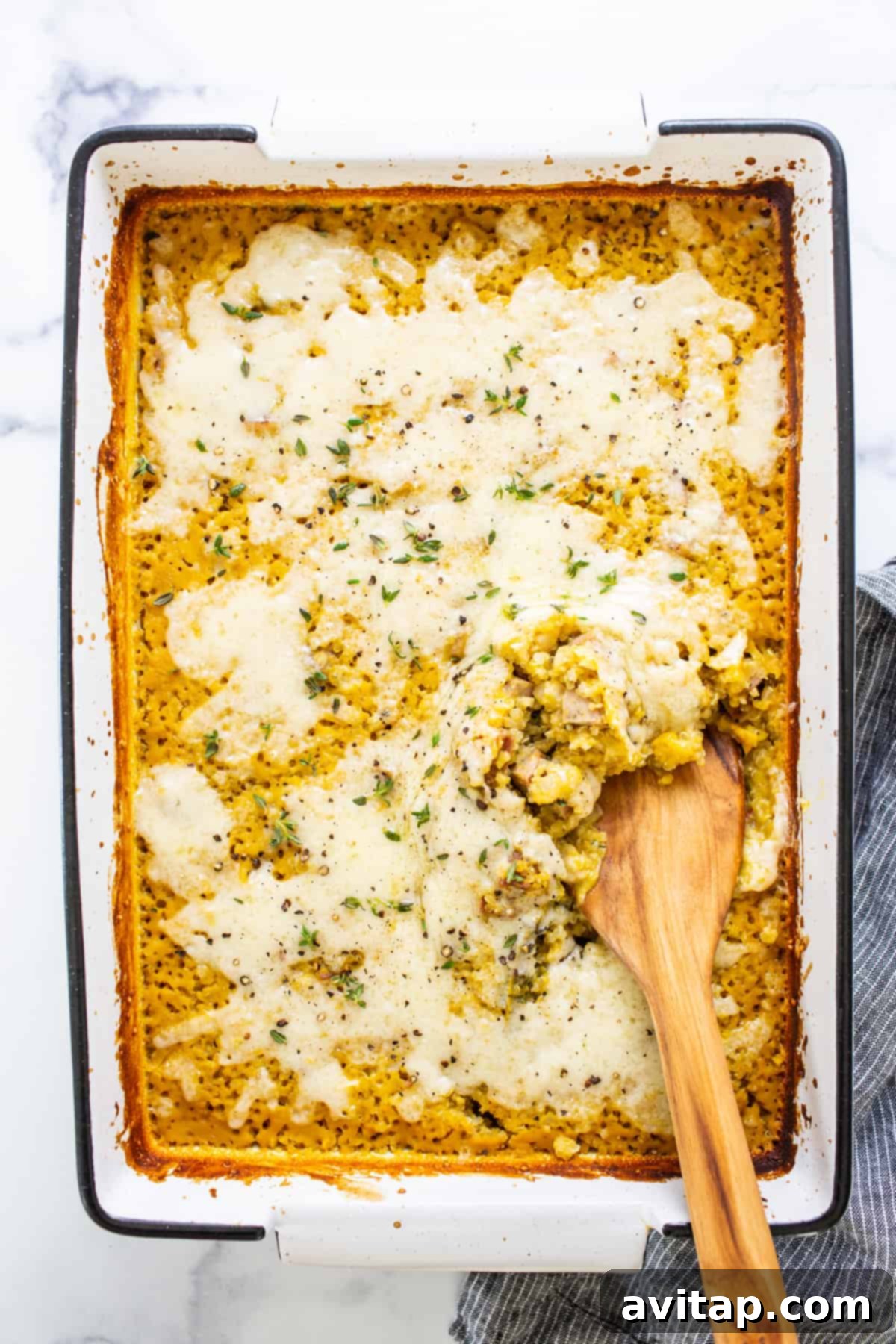 Cozy Butternut Quinoa Sausage Bake 2 A golden-brown butternut squash quinoa casserole with a wooden spoon inserted, showcasing the creamy texture and melted cheese topping.