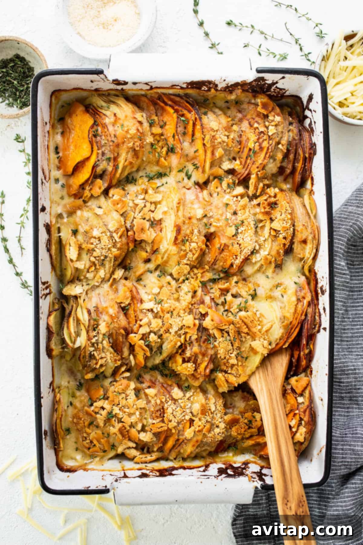 Sweet potato au gratin casserole in a baking dish with a wooden spoon, showcasing its cheesy, golden-brown top and crispy topping.