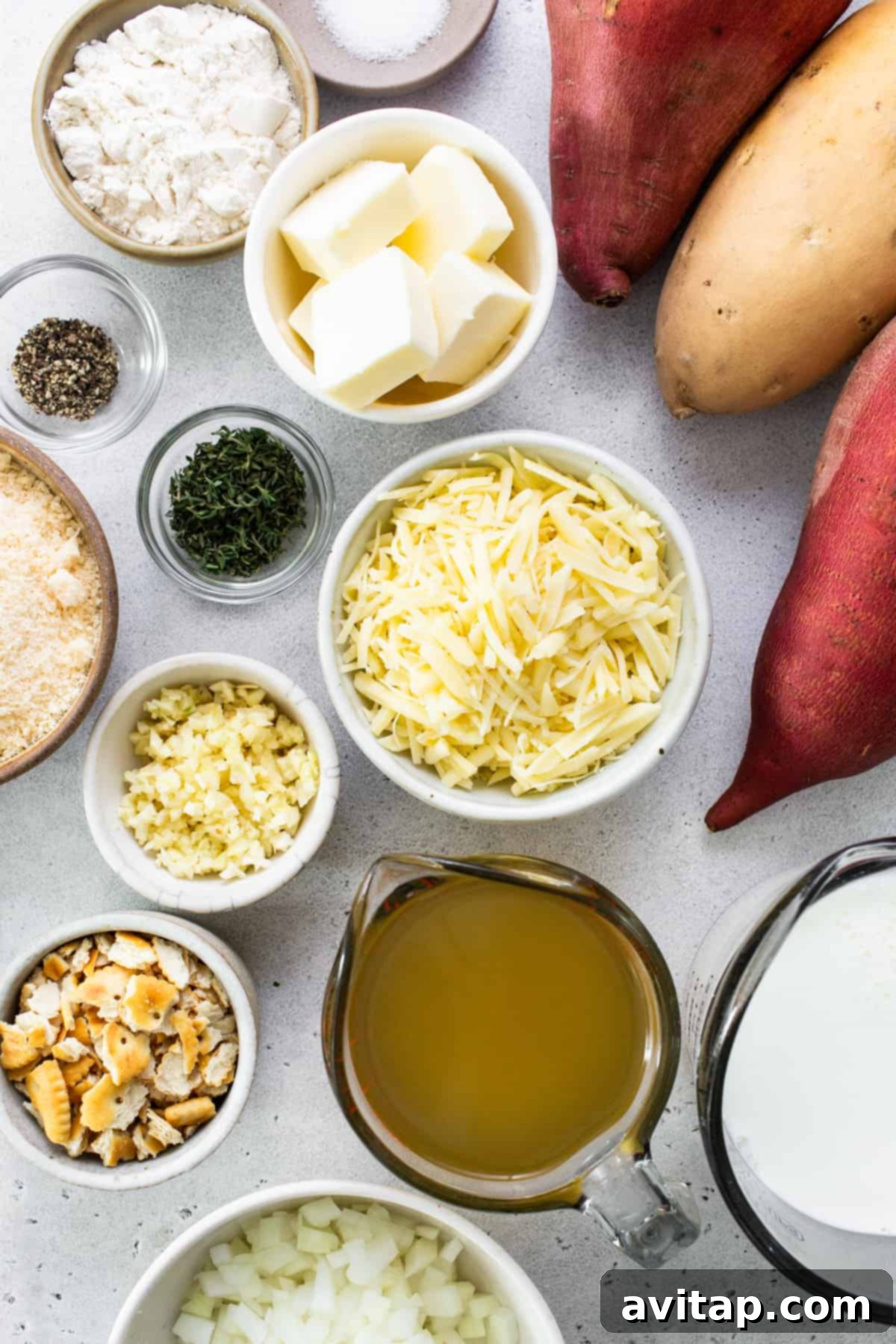A selection of fresh ingredients neatly arranged on a kitchen counter, including whole sweet potatoes, various cheeses, butter, herbs, and spices, all ready for the au gratin preparation.