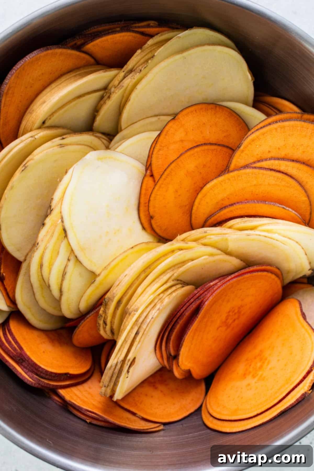 A bowl filled with uniformly thin and perfectly prepared sweet potato slices, ready for layering in an au gratin dish.