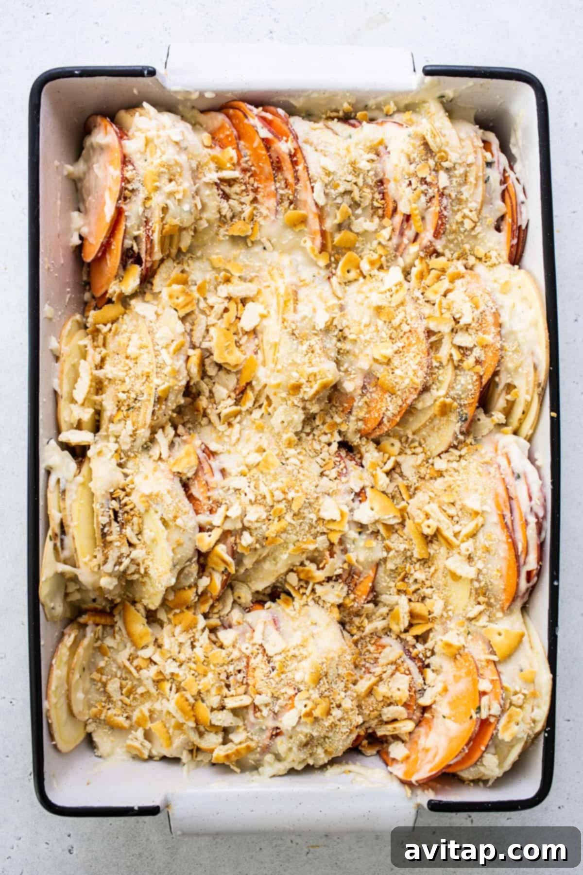 A baked sweet potato au gratin dish, golden and bubbly, with a scattering of fresh herbs on top, ready for serving.