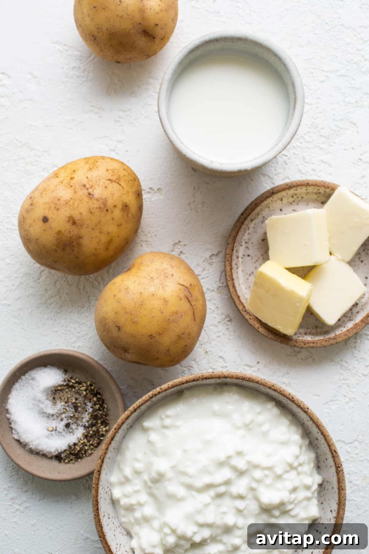 A vibrant and appealing selection of fresh, high-quality ingredients including golden Yukon gold potatoes, rich butter, creamy cottage cheese, wholesome milk, and essential salt and pepper, all meticulously arranged and ready for crafting delicious whipped mashed potatoes.
