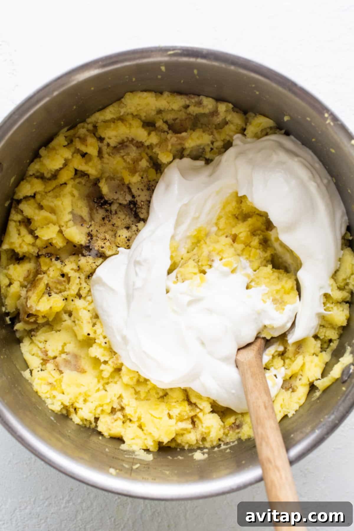 A clean mixing bowl containing a creamy batter or beautifully whipped ingredients, accompanied by a natural wooden spoon, symbolizing the careful and precise preparation process of a delicious, homemade dish.