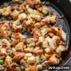 A skillet filled with fully prepared stuffing, incorporating sausage, bread cubes, and vegetables.