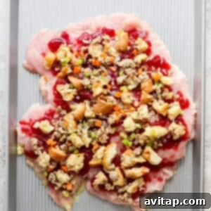 A butterflied turkey breast on a baking sheet, with cranberry sauce and stuffing spread over it, ready for rolling.