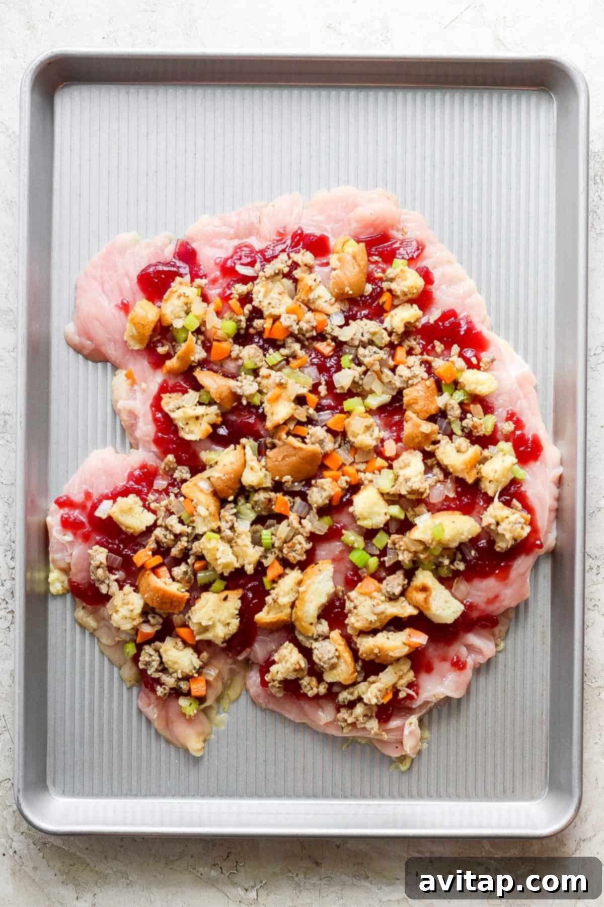 A baking sheet with a turkey roulade and cranberry topping, beautifully assembled and ready for roasting in the oven.