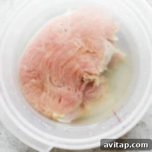 A turkey breast soaking in a clear brine solution in a large bowl.