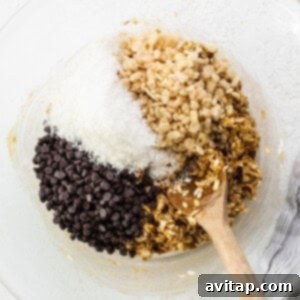 A bowl of granola and chocolate chips being stirred with a wooden spoon.