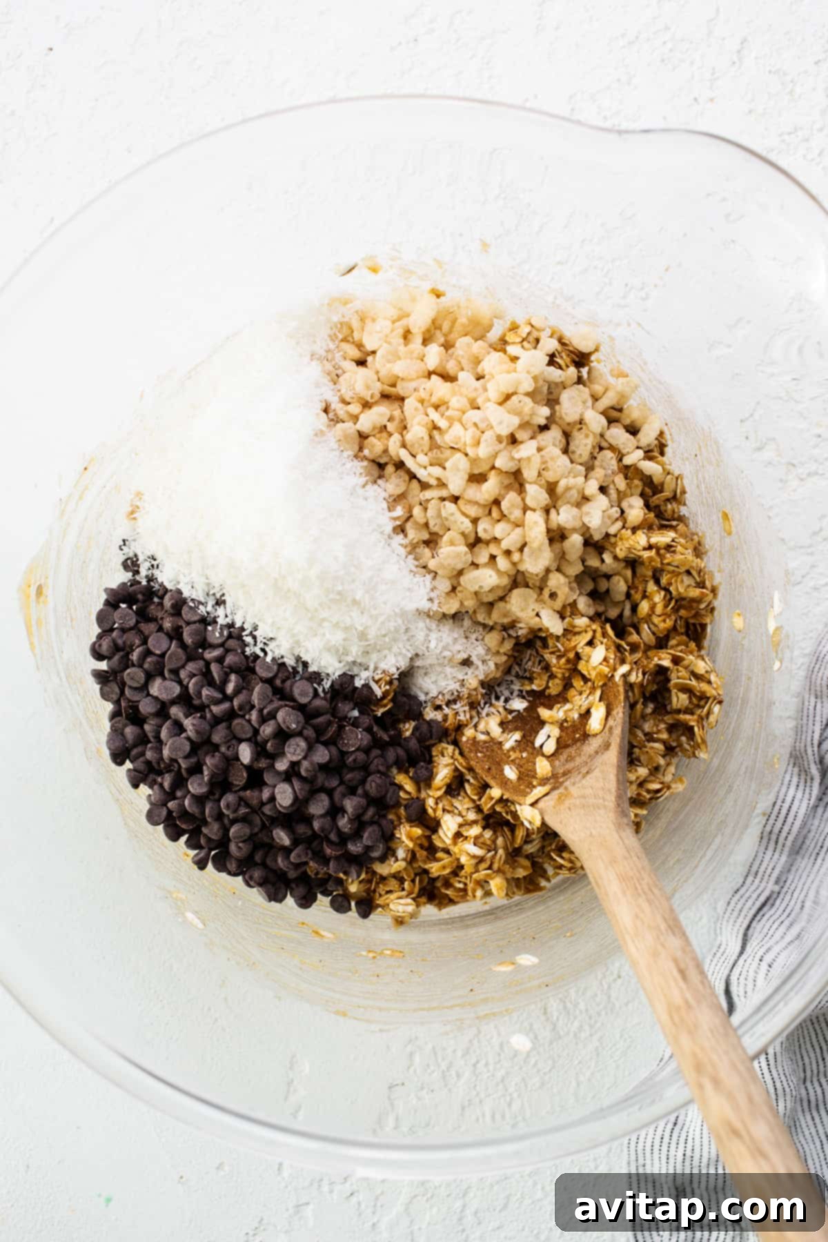 A bowl filled with crunchy granola and chocolate chips, accompanied by a wooden spoon.