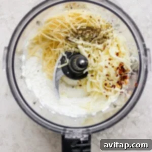 A food processor containing whipped cottage cheese, shredded Parmesan and mozzarella, red pepper flakes, and Italian seasoning, ready to be blended for the pasta topping.
