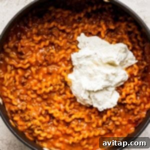 The one-pot lasagna pasta in a large pan, with creamy blended cheese being mixed in, creating a rich and cohesive dish.