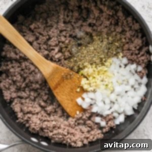 Sautéing ground beef, onions, and garlic in a large pan with a wooden spoon.