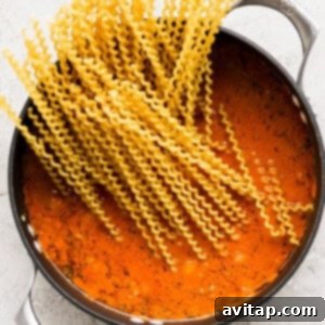 Long spaghetti noodles simmering in a rich tomato meat sauce in a large pot, being stirred gently.