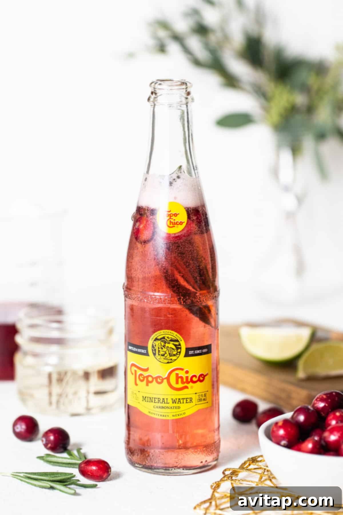 A bottle of cranberry juice with fresh cranberries and sprigs of rosemary, set against a festive backdrop.