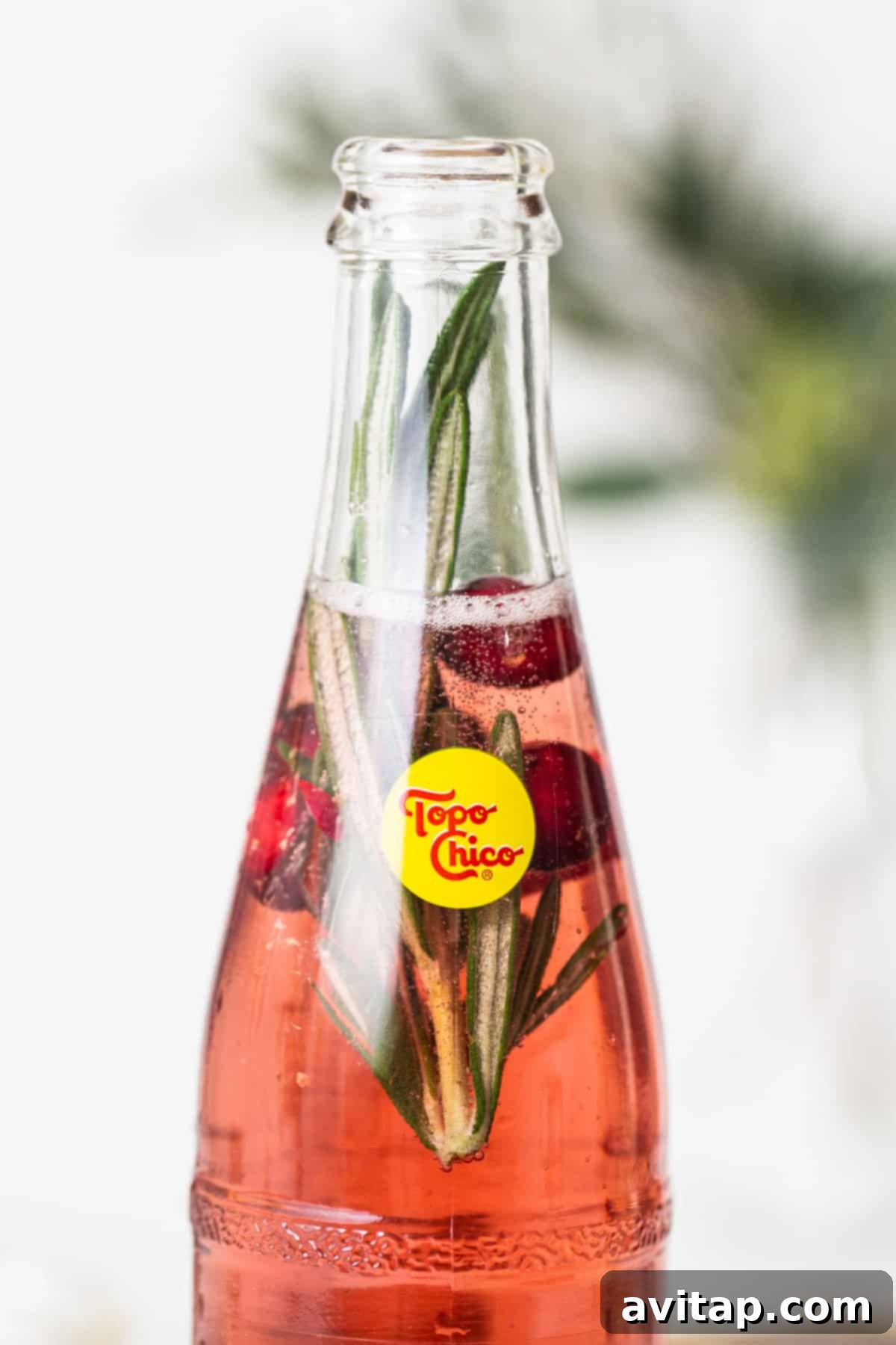 A bottle of soda with cranberry juice and sprigs of rosemary, showcasing the elegant presentation.