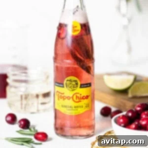 A bottle of cranberry soda with cranberries and sprigs of rosemary, ready to serve.
