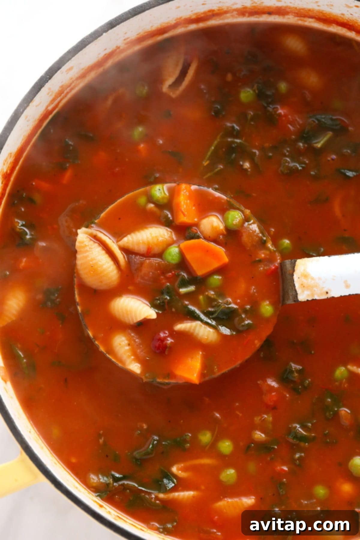 Make this vegetable packed minestrone soup and eat it all week long! A ladle scooping a generous portion of minestrone soup, showcasing the rich broth and variety of vegetables.