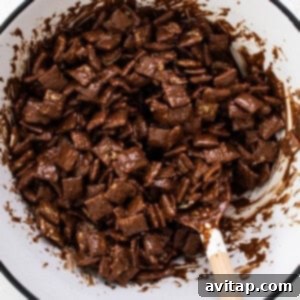 A bowl of chocolate-coated Chex cereal being stirred with a wooden spoon, showcasing the second layer of coating.