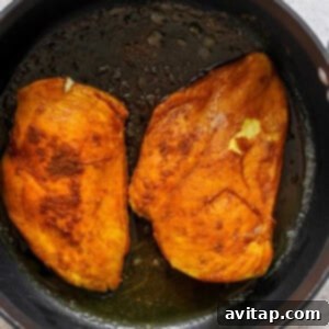 Two seared chicken breasts in a hot skillet, developing a golden crust.