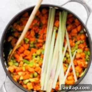 A pan with a colorful mix of carrots, onions, celery, and sweet potatoes sautéing to build the soup's flavor base.