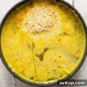 A pot of chicken and orzo soup simmering on the stove, with the pasta cooking through.