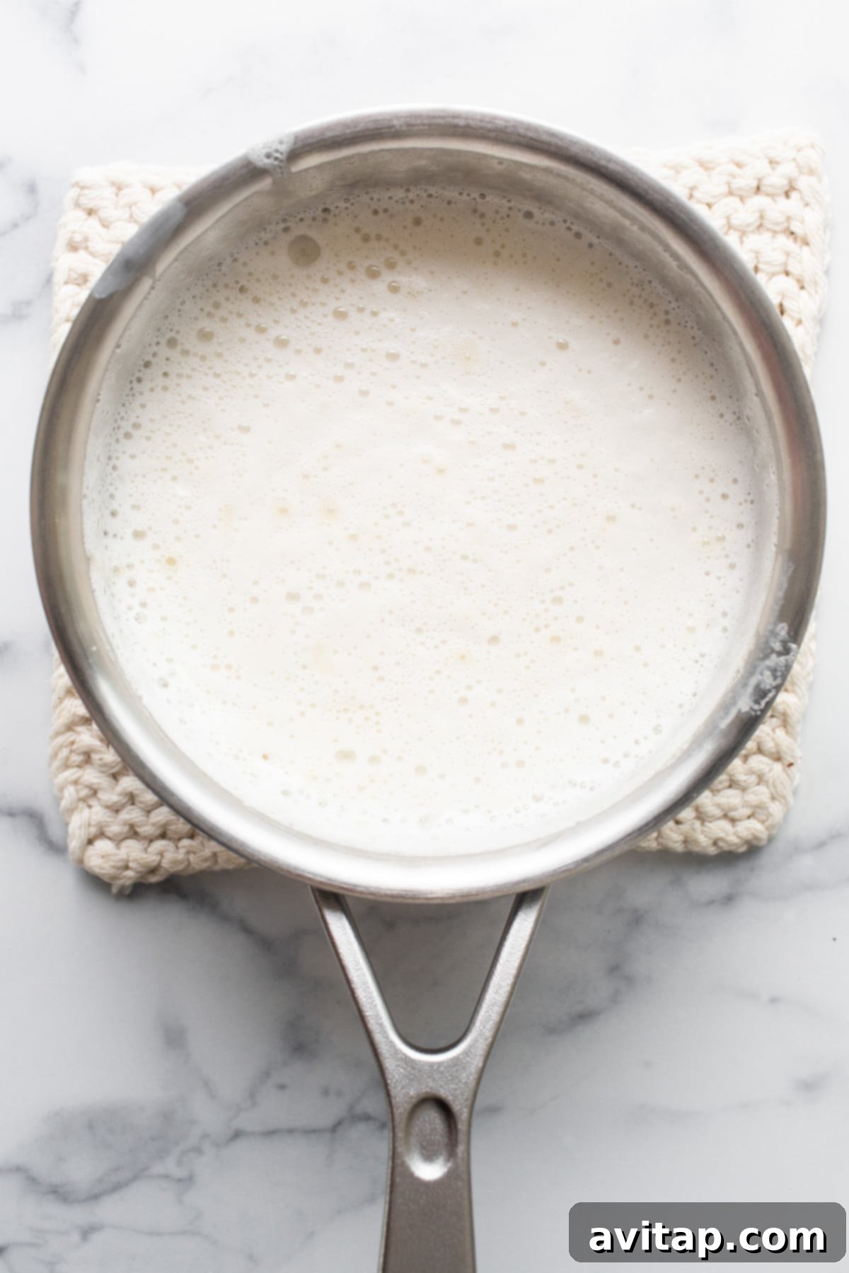 A saucepan filled with milk on a marble countertop, ready for heating to prepare the panna cotta base.
