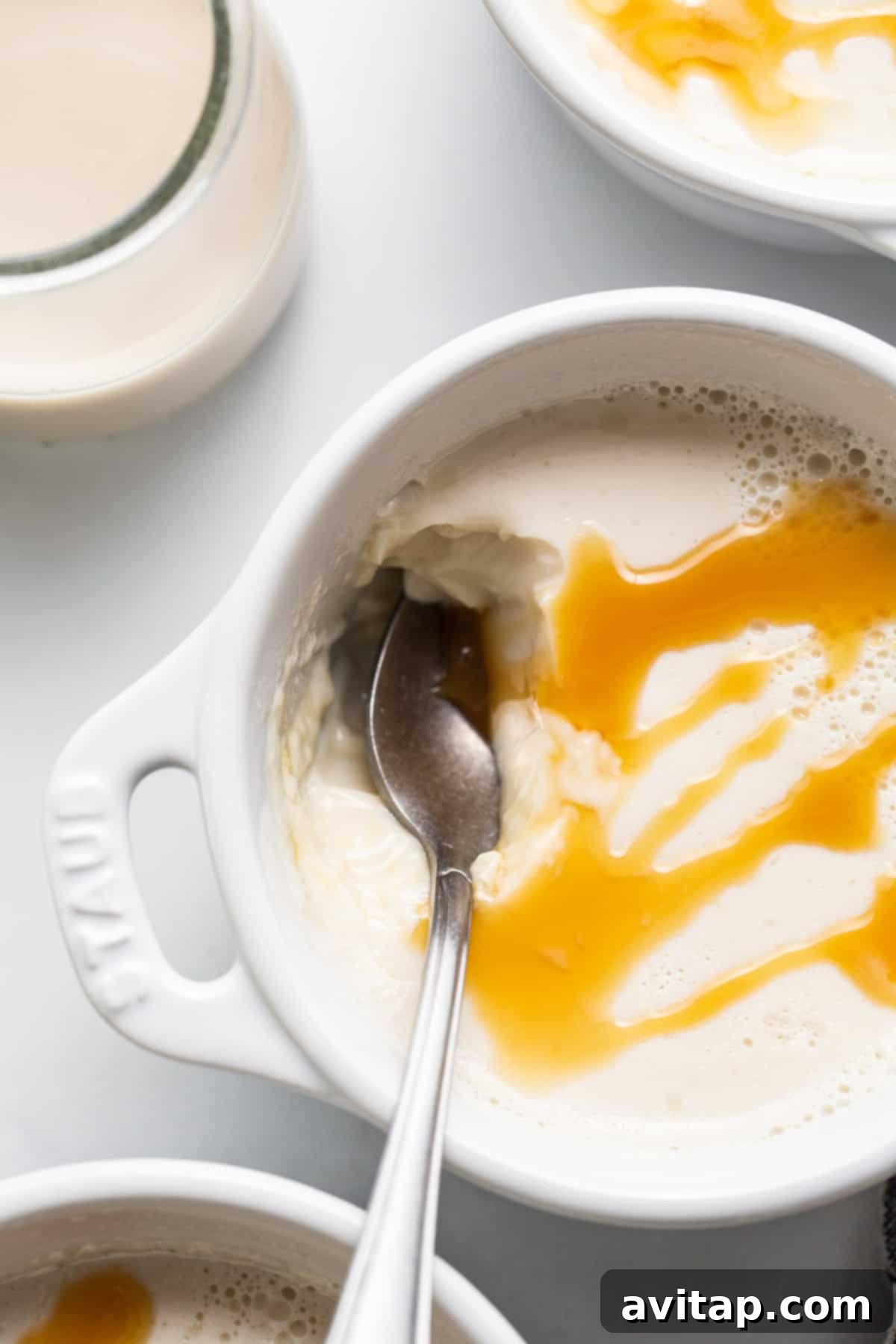 A delightful bowl of creamer panna cotta, topped with a generous swirl of caramel sauce and a spoon.