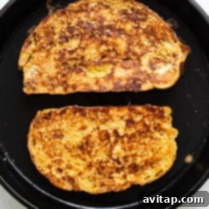 Two slices of french toast cooking in a skillet, turning golden brown.