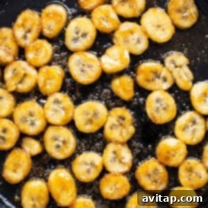 Sliced bananas are being sautéed in a skillet, creating the caramelized topping.