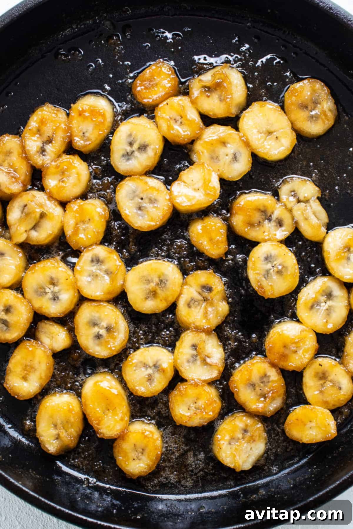 Sliced bananas are being fried in a skillet, caramelizing in a rich sauce.