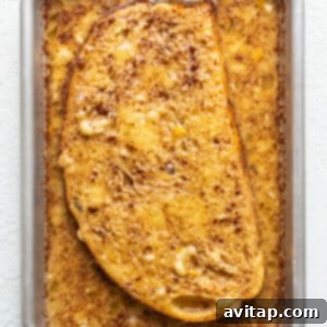 A slice of french toast soaking in the egg mixture in a pan.