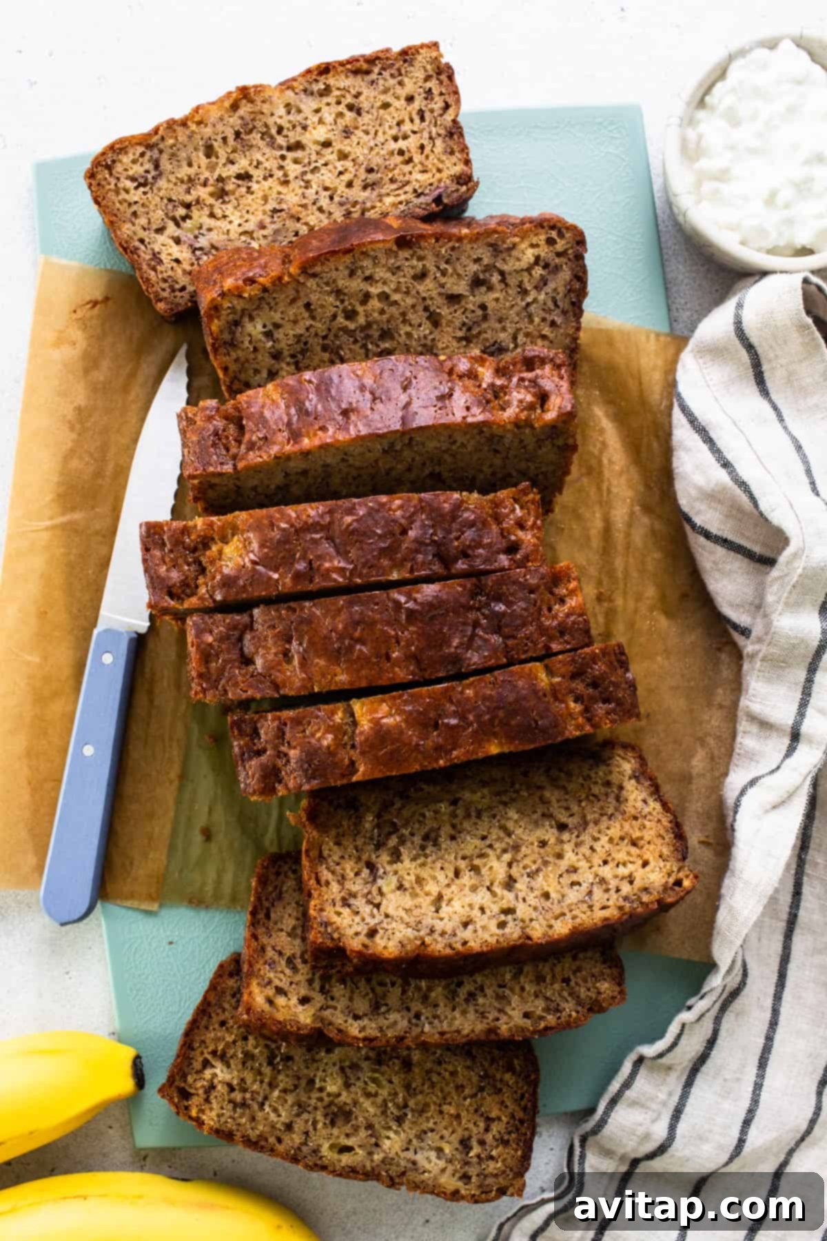 A beautifully sliced loaf of protein banana bread on a wooden cutting board, with a knife resting beside it.