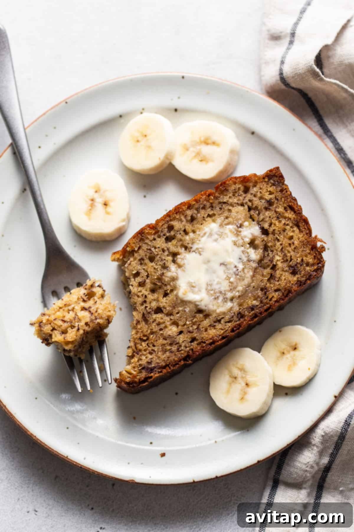 A close-up of a single slice of protein banana bread on a white plate with a fork, ready to be eaten.