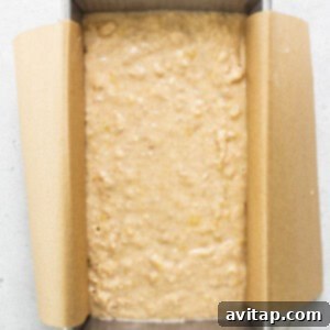 Banana bread batter in a loaf pan, ready for baking on a white surface.