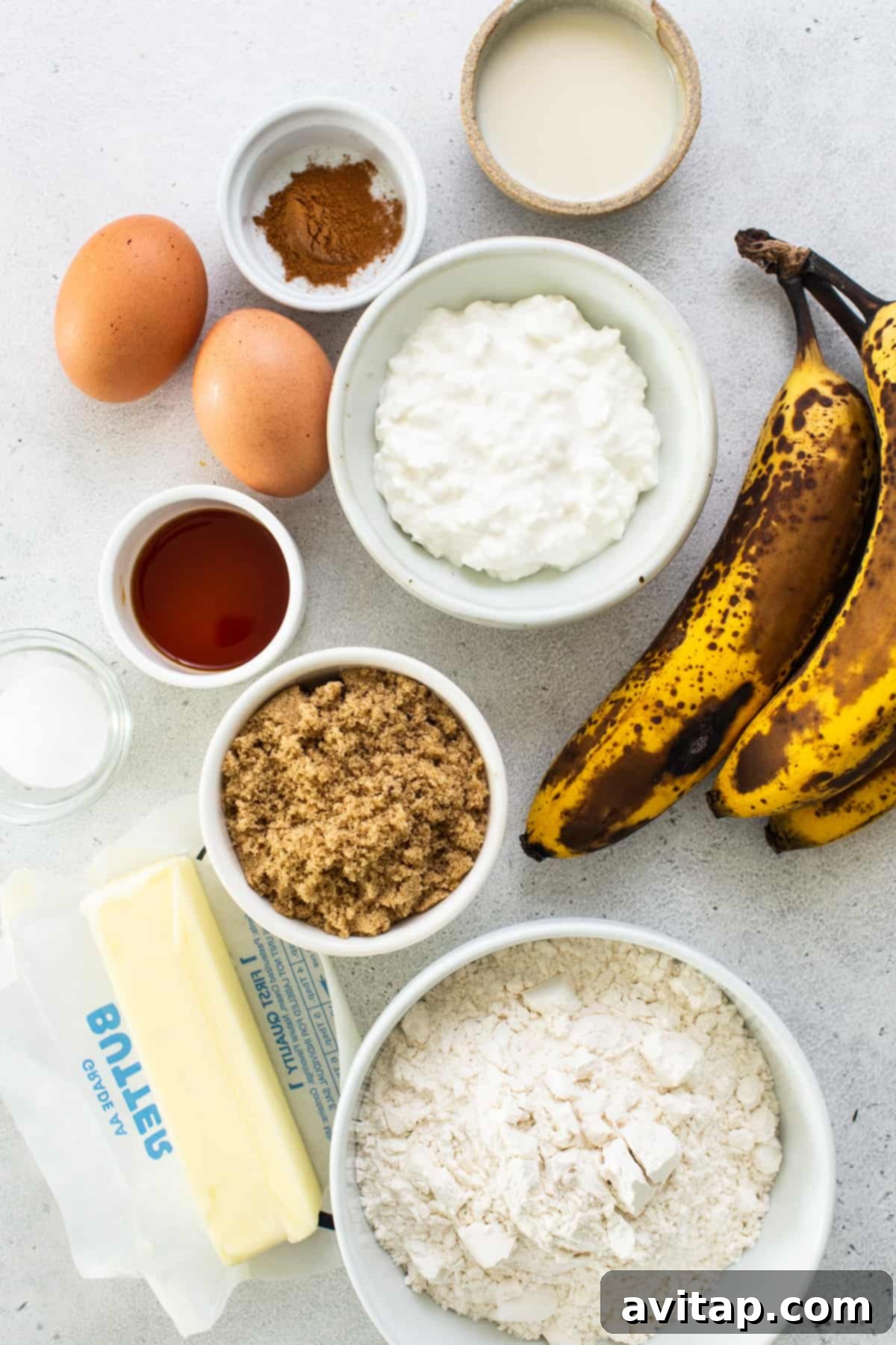 A selection of fresh ingredients laid out for making banana bread, including ripe bananas, flour, eggs, and butter.